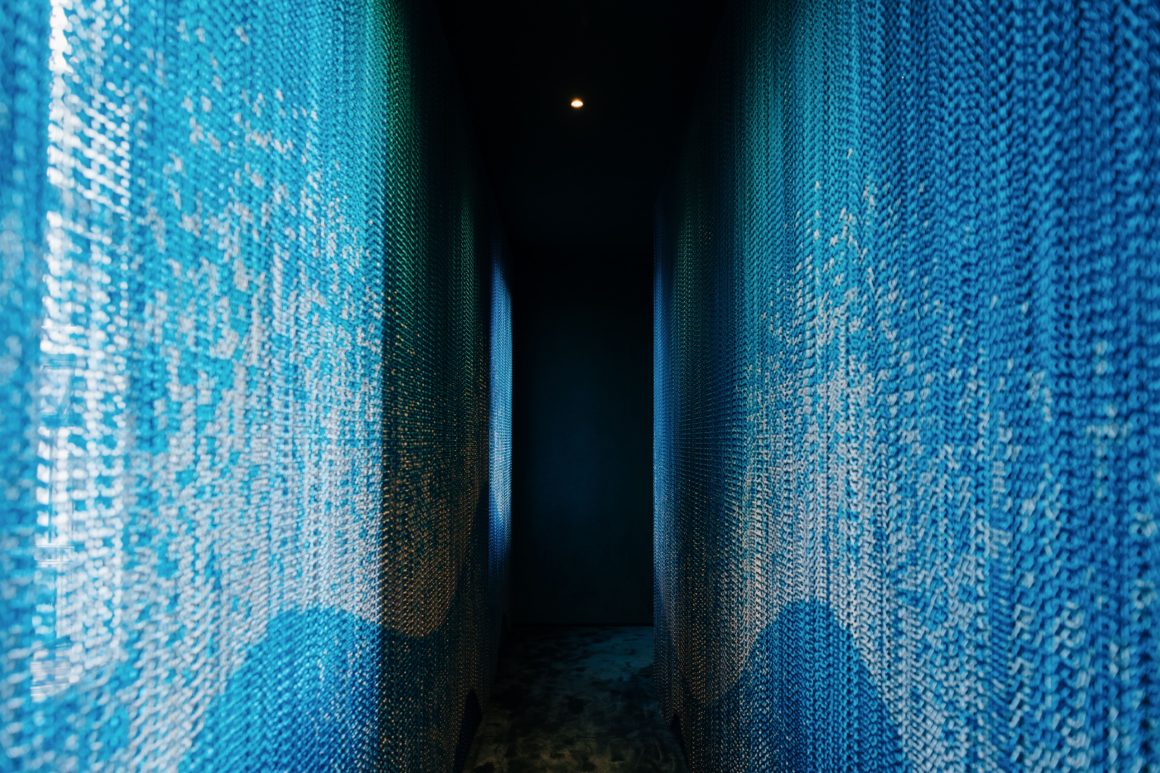 Dettaglio dell'installazione Kriskadecor ad Archiproducts Milano, con catene in alluminio blu che catturano la luce in uno spazio immersivo.