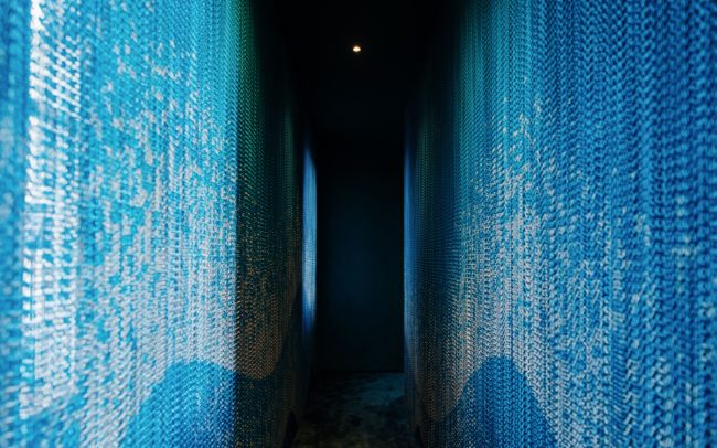 Dettaglio dell'installazione Kriskadecor ad Archiproducts Milano, con catene in alluminio blu che catturano la luce in uno spazio immersivo.
