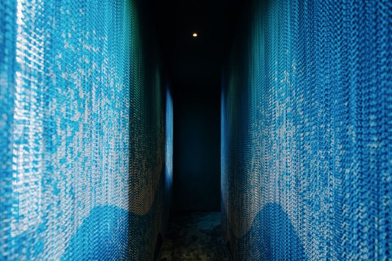 Dettaglio dell'installazione Kriskadecor ad Archiproducts Milano, con catene in alluminio blu che catturano la luce in uno spazio immersivo.